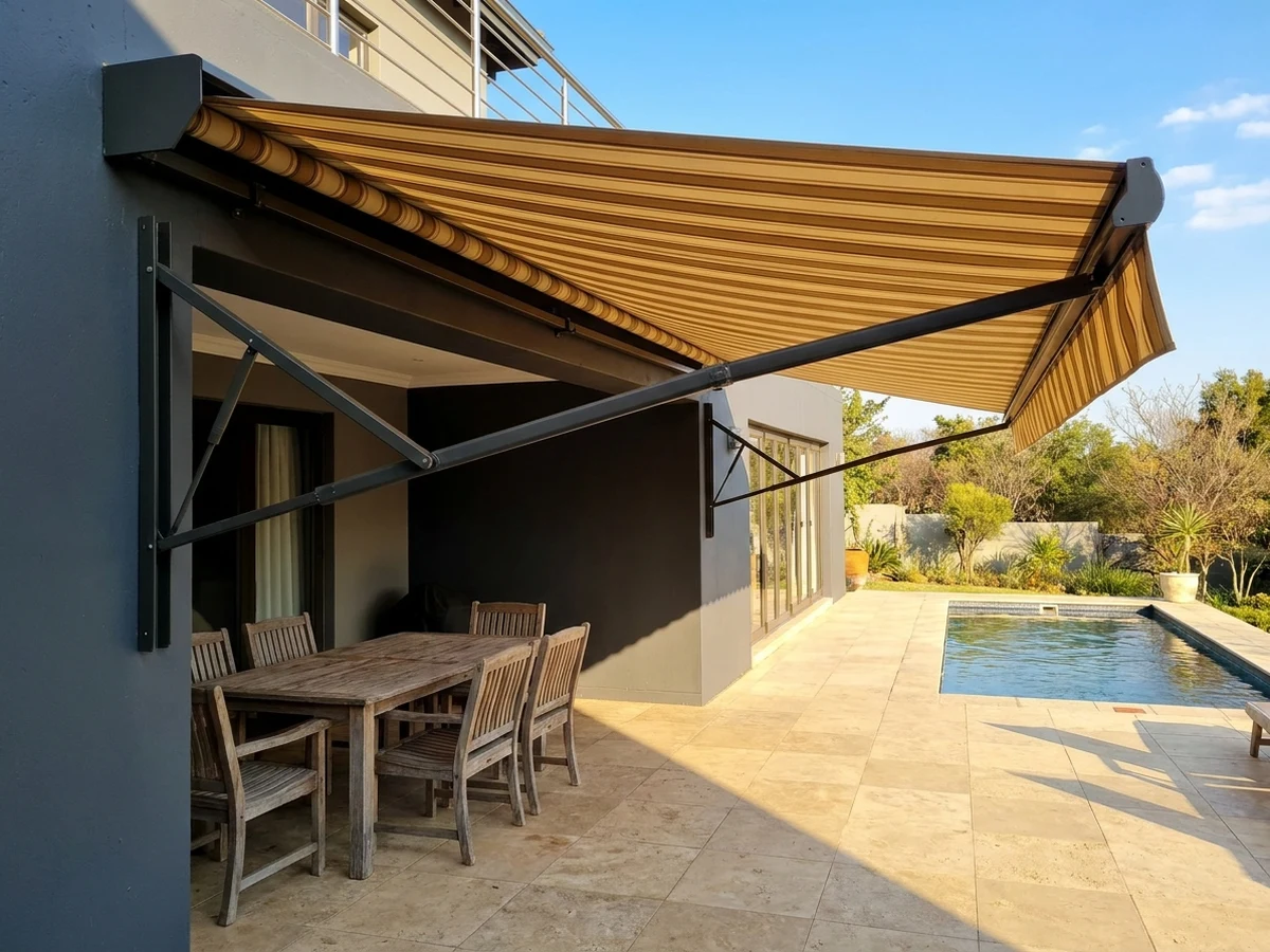 Folding-arm awning fully extended over a Bryanston braai terrace, a crisp line of afternoon shade falling across the paving and dining table